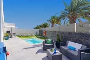 Relax by the pool surrounded by a stone wall, lounge chairs, and a dining area.