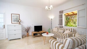 A living room with a striped sofa, a television, a small table, and a bookshelf. - Villa Mistral Cottage by Villa Plus (Ionian Islands)