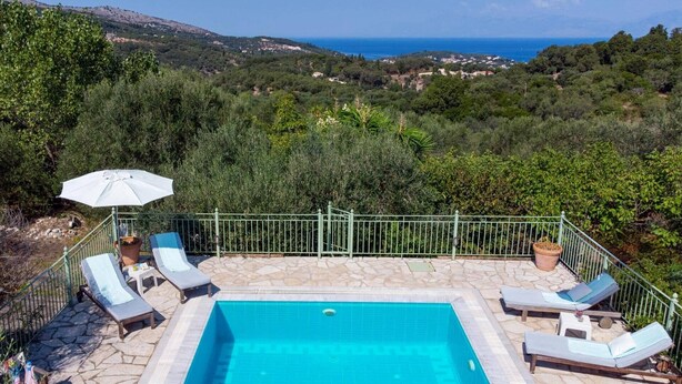 A pool area with a view of the sea, surrounded by greenery and a metal fence. - Villa Mistral Cottage by Villa Plus (Ionian Islands)