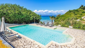 Ein Schwimmbecken mit Liegestühlen und Blick aufs Meer.