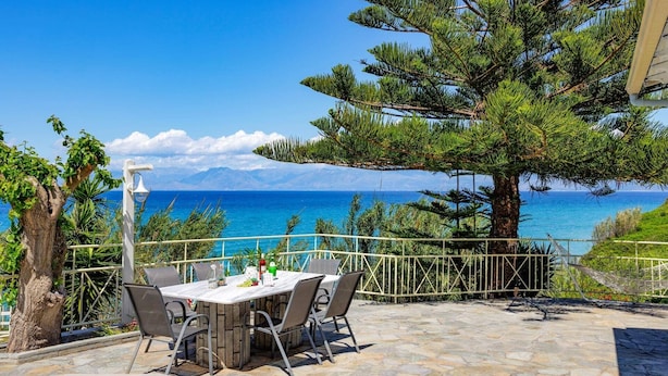 Ein Essbereich im Freien mit Tisch und Stühlen, mit Blick auf eine schöne Aussicht auf Meer und Berge.