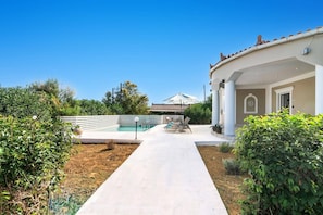 A pool area with a clear walkway leading to a building with a tiled roof.