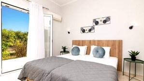 A bedroom with a large bed, a wooden headboard, two wall-mounted lights, a view of greenery outside, and a ceiling fan.