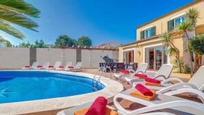 Zona de piscina con sillones de descanso y toallas, una escultura de toro y un edificio con techo de tejas.