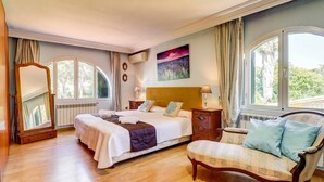 Un dormitorio con cama, mesitas de noche, una silla, un espejo y una ventana.