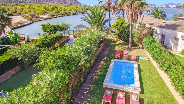 A pool area with a view of a lake and mountains, surrounded by lush greenery and palm trees.