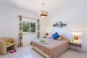 A bedroom with a bed, a chair, a window, and a bedside table with a lamp.