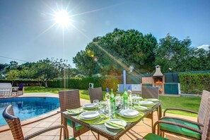 An outdoor dining area with a pool, wicker chairs, and a brick oven.
