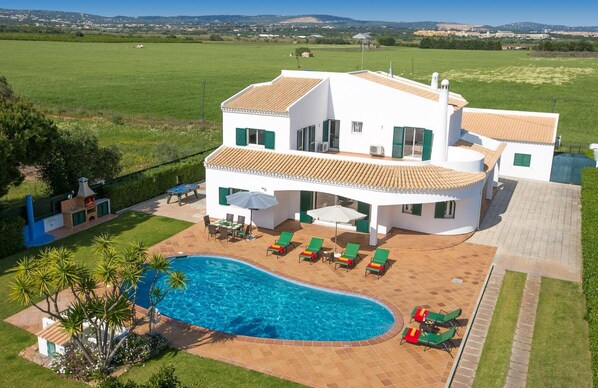 A white villa with a swimming pool, outdoor seating, and a view of the countryside.