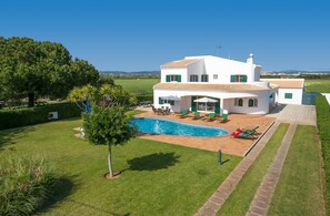 A white villa with a swimming pool, green lawn, and a view of the countryside.