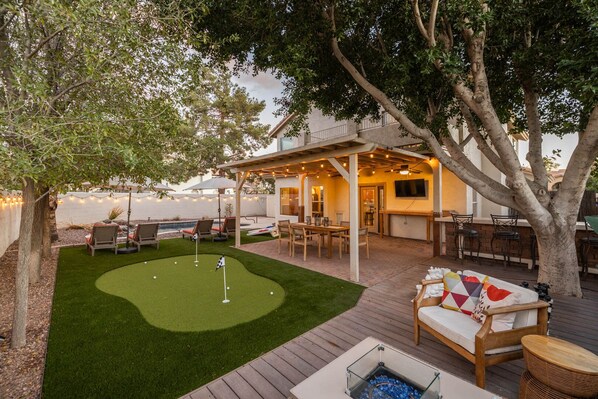 A backyard with a putting green, outdoor seating, and a pool. - Family Poolside Fun, Golf & Games! (Gilbert)