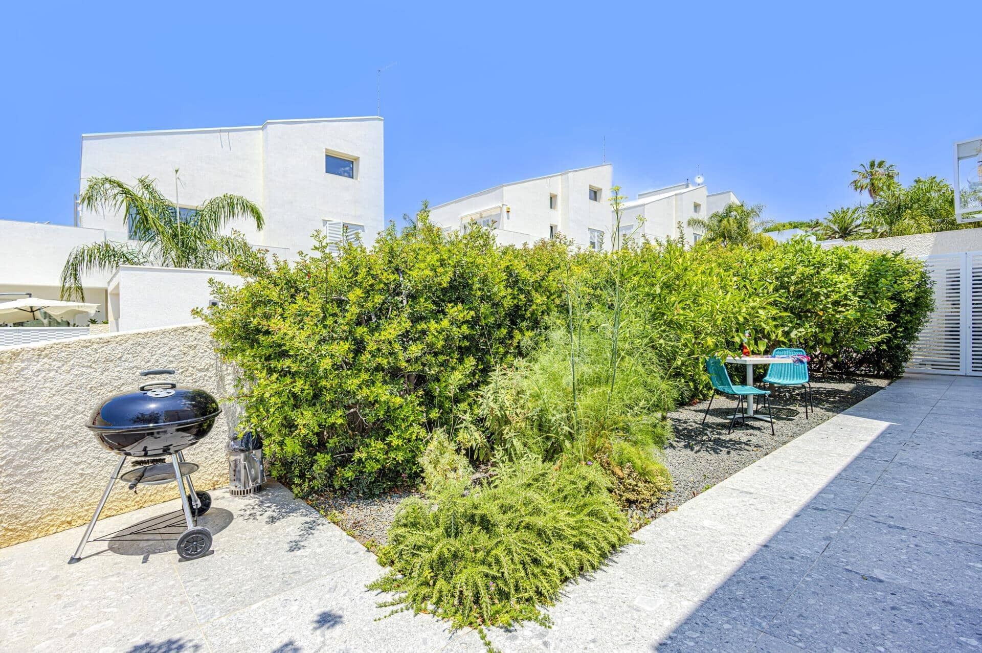 A patio area with a barbecue grill, outdoor seating, and lush greenery.