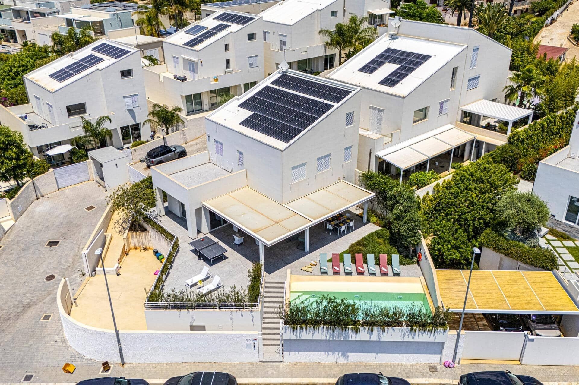 A modern residential building with multiple solar panels on the roof, a covered outdoor seating area, and a small pool.