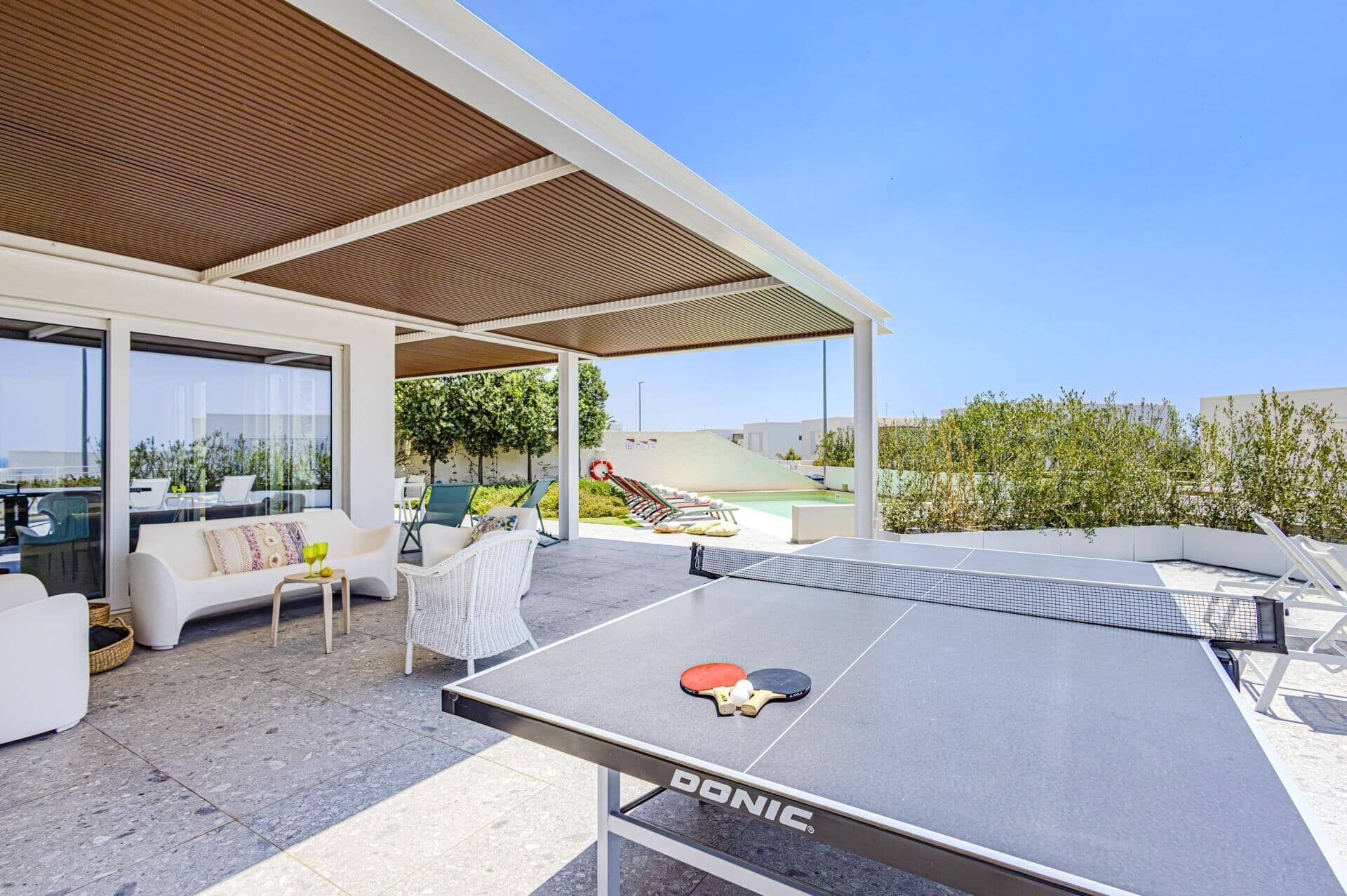 Un espace de détente extérieur moderne, avec une table de ping-pong, des sièges et une piscine en arrière-plan.