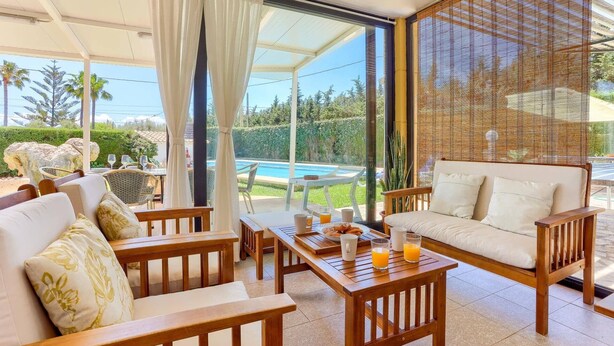 Une terrasse ensoleillée avec vue sur la piscine, du mobilier en bois et un espace salon abrité.