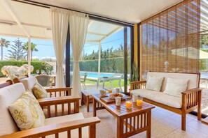 A sunlit patio with a pool view, wooden furniture, and a covered seating area. - Villa Victoria Musical by Villa Plus (Port de Pollença)