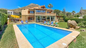 Une maison à deux étages avec une piscine, un espace salon extérieur et une vue sur les montagnes.