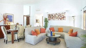 A living room with a grey sofa, orange cushions, a round coffee table, and a dining area with chairs and a table. - Villa Figueral by Villa Plus (Mallorca)