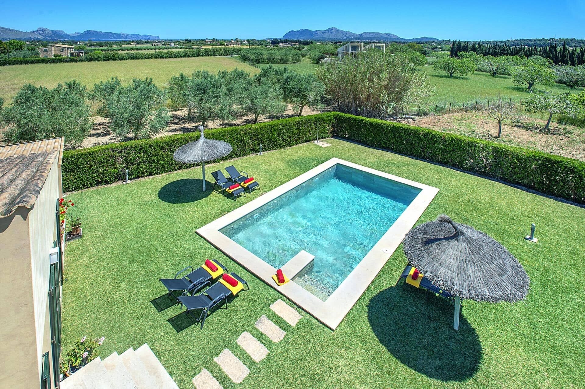 A rectangular swimming pool surrounded by a well-manicured lawn, with lounge chairs and umbrellas.