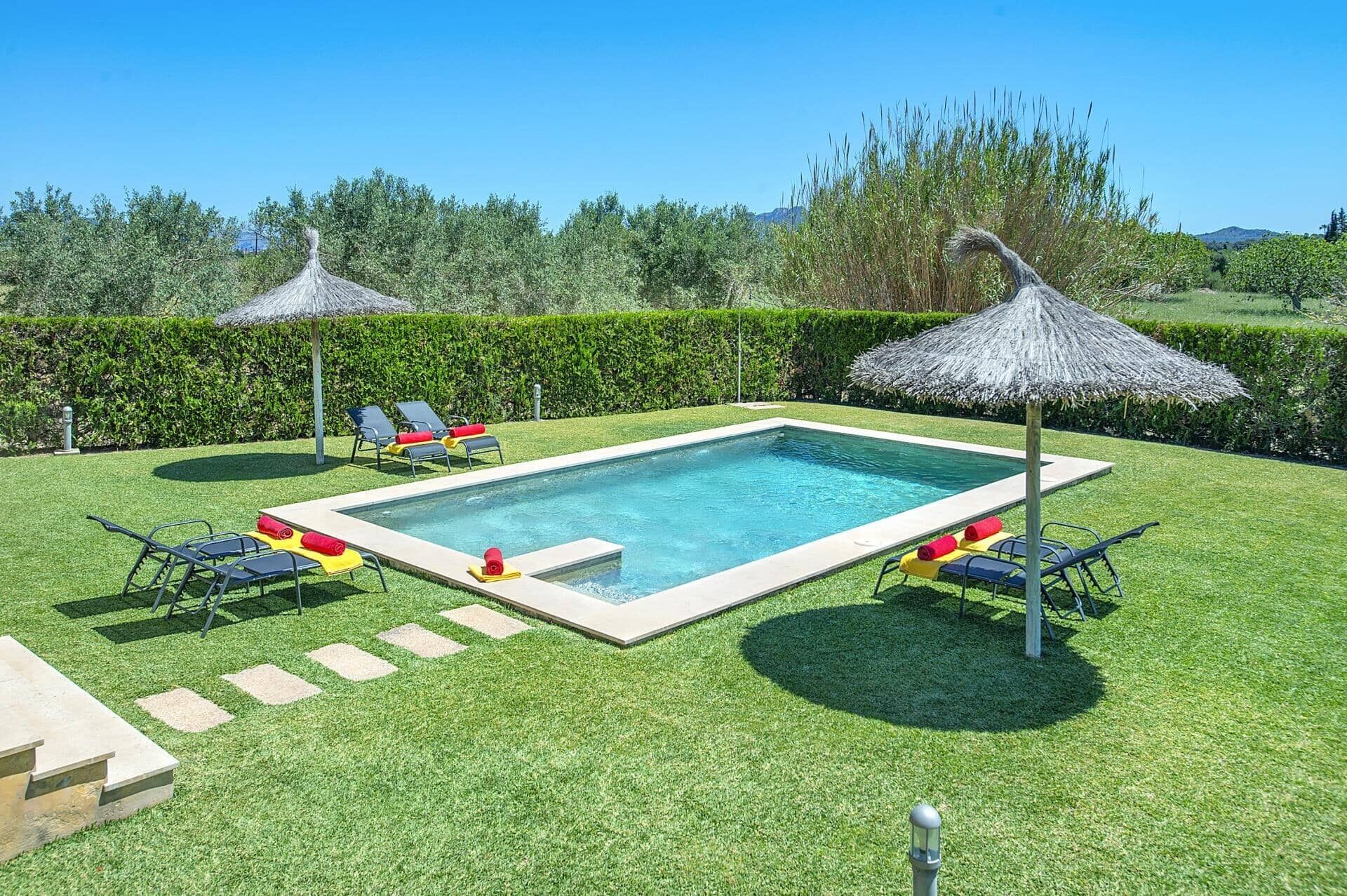 Una piscina rectangular con superficie de agua azul cristalina, rodeada por un césped cuidado y varias sillas de descanso.