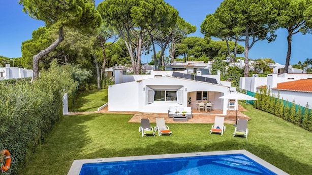 Una villa moderna con piscina, un patio con sillones de descanso y vistas a casas circundantes.