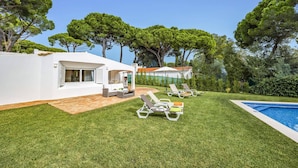 Una villa moderna con piscina, mobiliario de exterior y abundante vegetación.