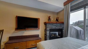 Une chambre d’hôtel avec une cheminée en pierre, un grand téléviseur à écran plat fixé au mur, un banc en bois et un lit.