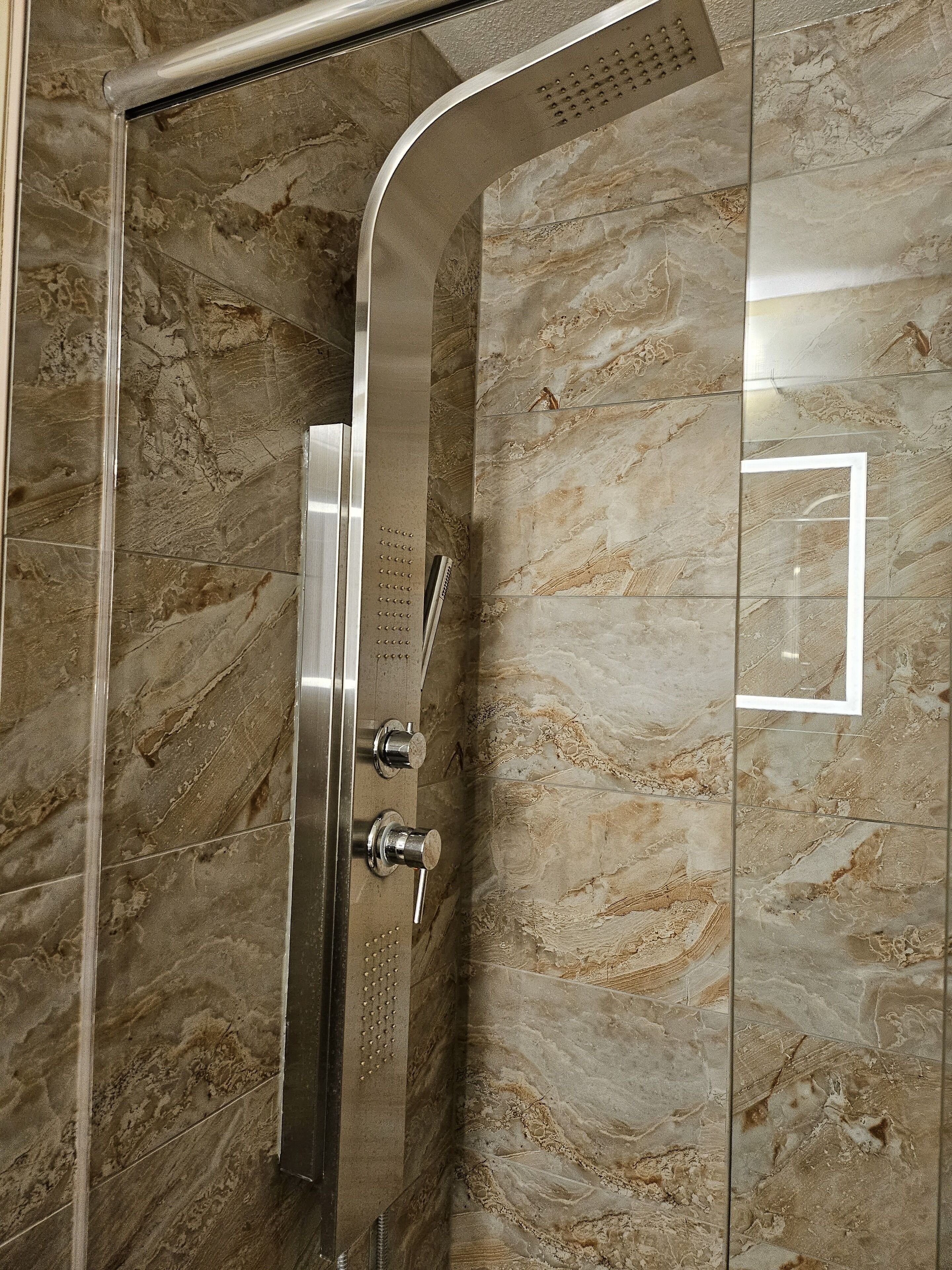 A modern shower enclosure with a curved showerhead and control knobs.