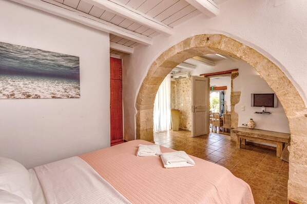 A bedroom with a bed, a painting, an arched doorway, a television, and a table.