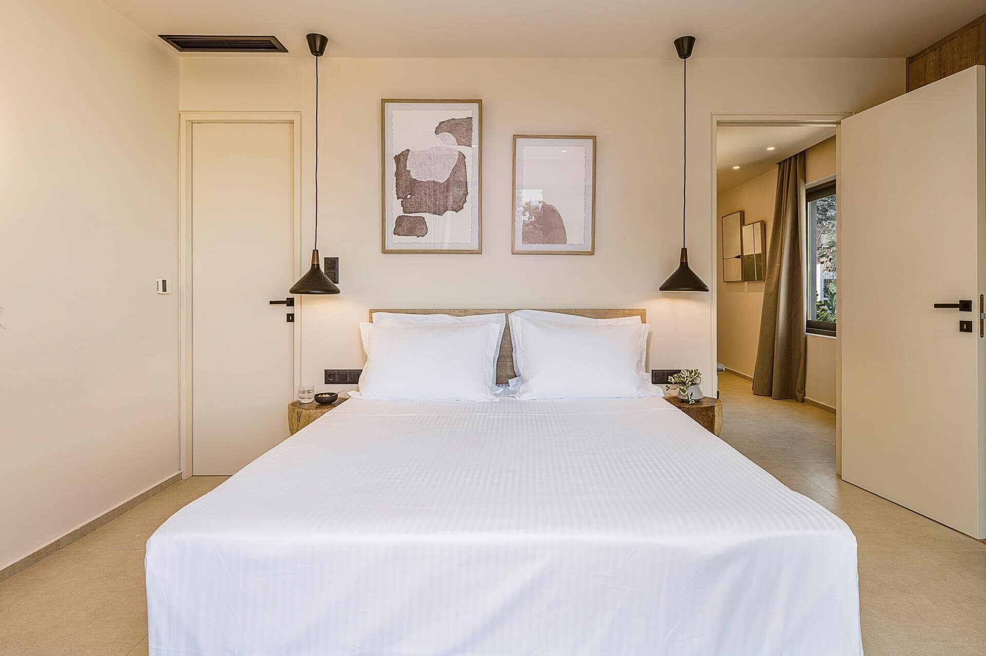 Habitación de hotel con una cama grande, dos mesitas de noche, una lámpara de pared y dos obras de arte enmarcadas.