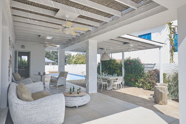 Un espace extérieur aménagé avec un coin salon couvert, des meubles en osier, une piscine et une table à manger.