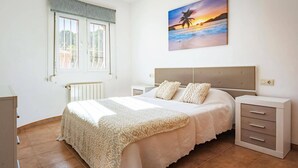 Een slaapkamer met een groot bed, een nachtkastje, een dressoir en een schilderij van een zonsondergang boven de oceaan.