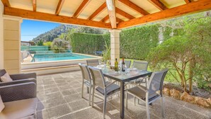 A covered outdoor area with a pool, dining table, chairs, and a sofa. - Villa Rabasso by Villa Plus (Pollença)