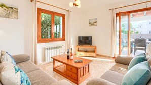 Un salon comprenant un canapé, une table basse, un téléviseur posé sur un meuble en bois et une fenêtre donnant sur un paysage verdoyant.