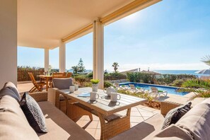 A covered outdoor seating area with a pool and ocean view. - Villa India II by Villa Plus (Sant Lluís)