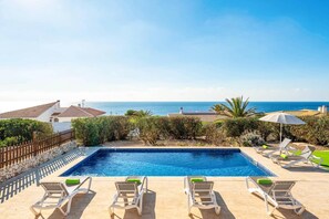 A swimming pool with lounge chairs and umbrellas, overlooking a coastal view. - Villa India II by Villa Plus (Sant Lluís)