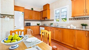 A kitchen with wooden cabinets, a microwave, a sink, and a window with a view of greenery.