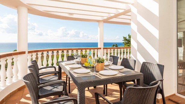 A covered outdoor dining area with a table set for four, overlooking the ocean. - Villa Casa Bonita by Villa Plus (Alayor)