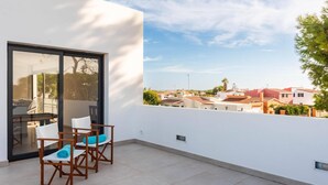Un balcon avec une table et des chaises, une porte vitrée et une vue sur les maisons voisines.