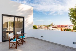 Un balcon avec une table et des chaises, une porte vitrée et une vue sur les maisons voisines.