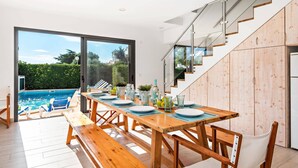 Un espace repas moderne avec une table en bois disposée pour quatre personnes, donnant sur une piscine et un jardin luxuriant.