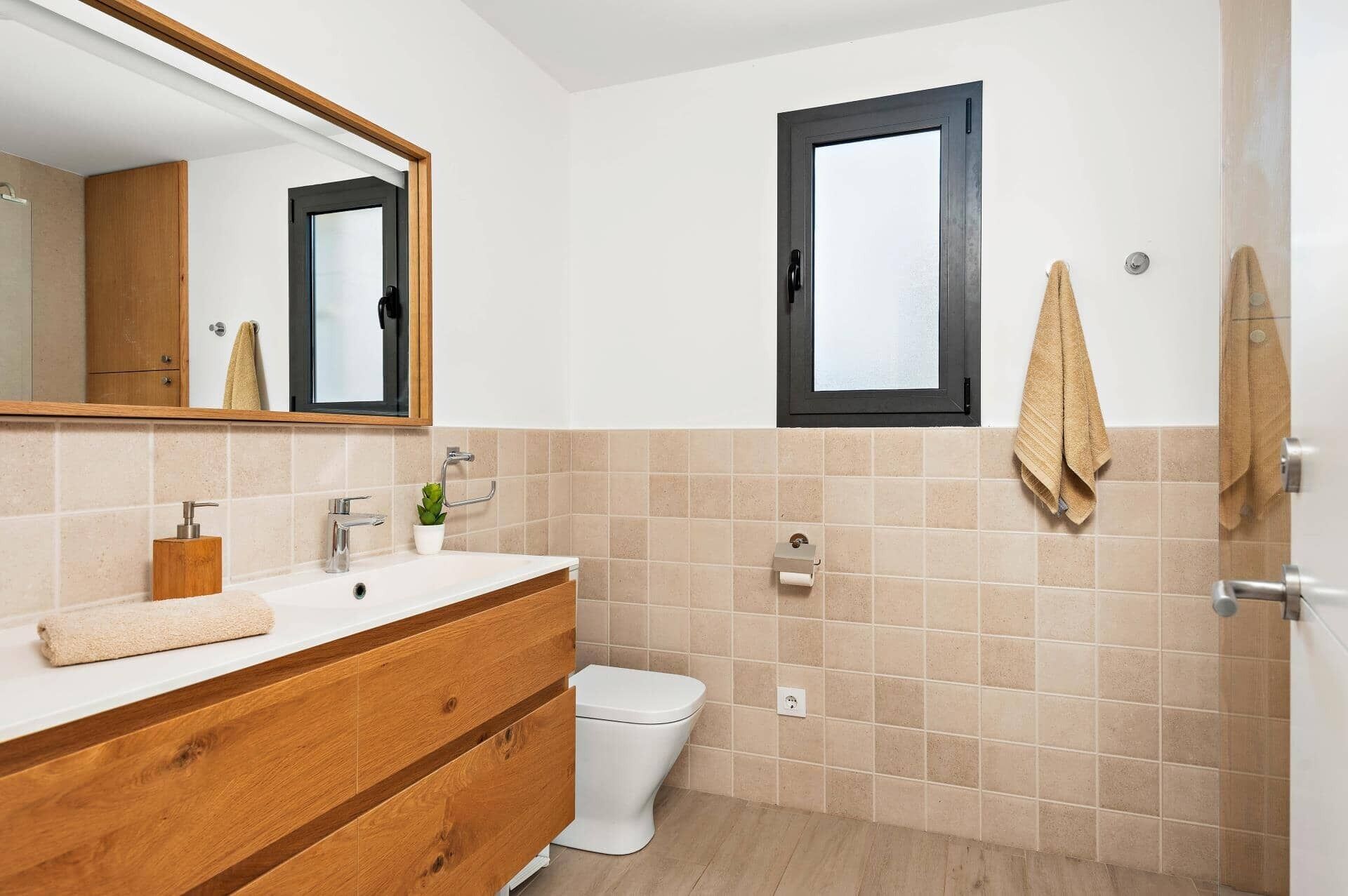 Un baño con tocador de madera, inodoro blanco y espejo sobre el lavabo.