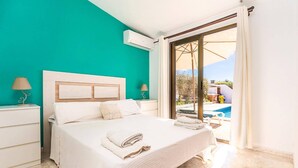 A bedroom with a bed, a nightstand, a lamp, and a view of a pool. - Villa Shambala by Villa Plus (Cala en Porter)