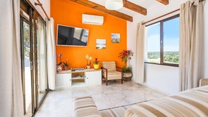 A room with a TV, a chair, a sofa, and a window with a view. - Villa Shambala by Villa Plus (Cala en Porter)
