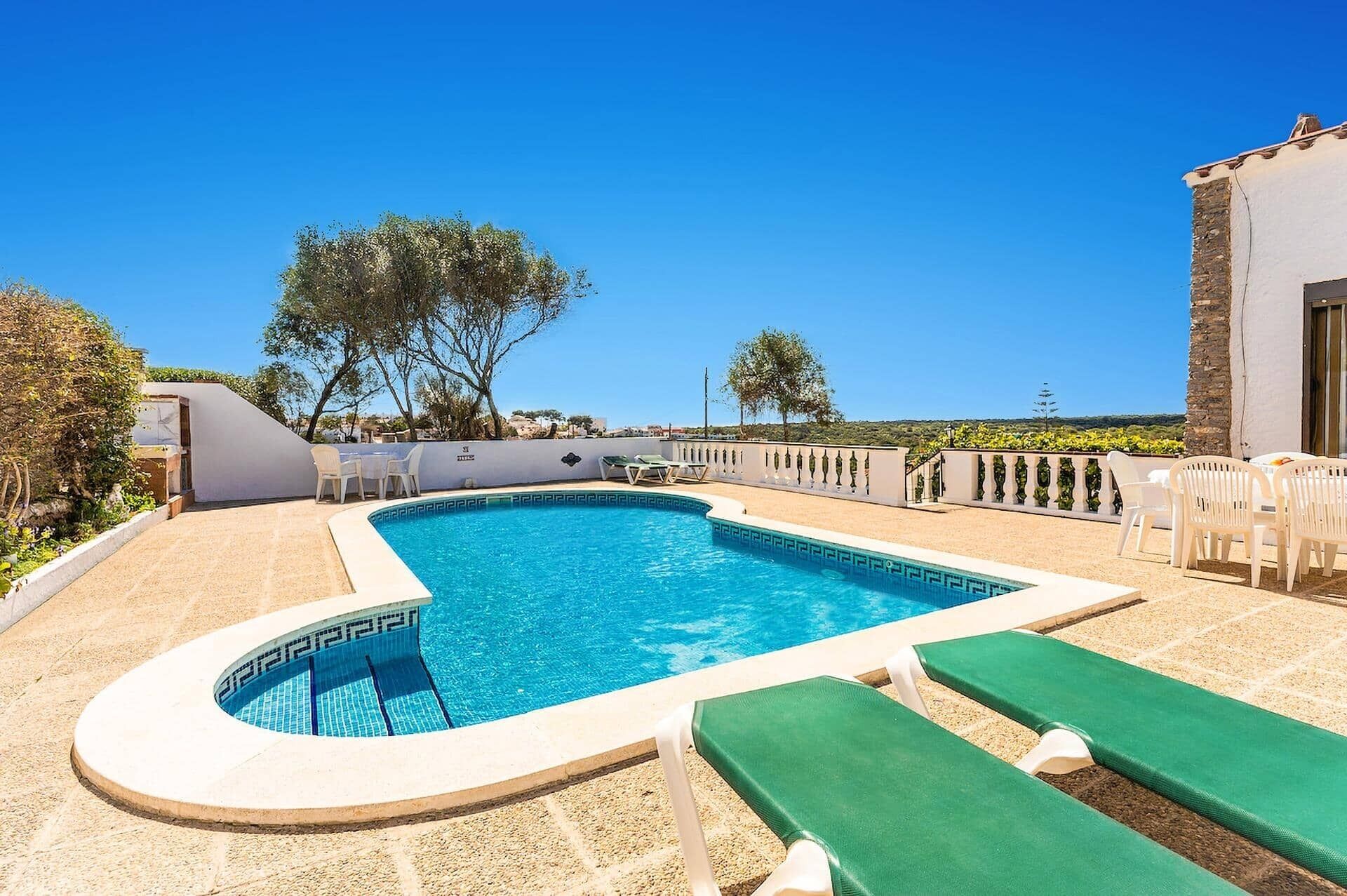 A swimming pool with a curved edge, surrounded by lounge chairs and a stone wall.