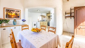 A dining area with a table set for two, a kitchen visible through an archway, and a wooden ceiling. - Villa Shambala by Villa Plus (Cala en Porter)