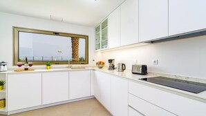 A modern kitchen with white cabinets, a large window with a view, a countertop with a coffee maker, and a toaster.
