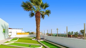A rooftop garden with artificial grass, a palm tree, and a white building.