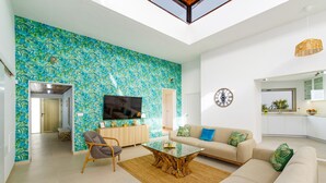 A spacious living room with a large TV, a sofa, a coffee table, and a wall with a tropical leaf pattern.