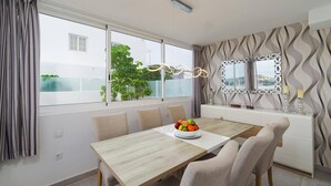 Een eetgedeelte met een houten tafel, beige stoelen, een fruitschaal en een decoratieve spiegel aan de muur.